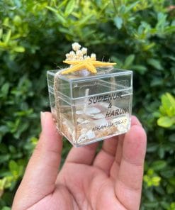 Deniz Esintisiyle Unutulmaz Anılar... Şeffaf mika kutuda sunulan, deniz kabukları ve nazar boncuğuyla süslenmiş özel tasarım mumlarımız; söz, nişan ve düğünleriniz için zarif bir hatıra olacak.